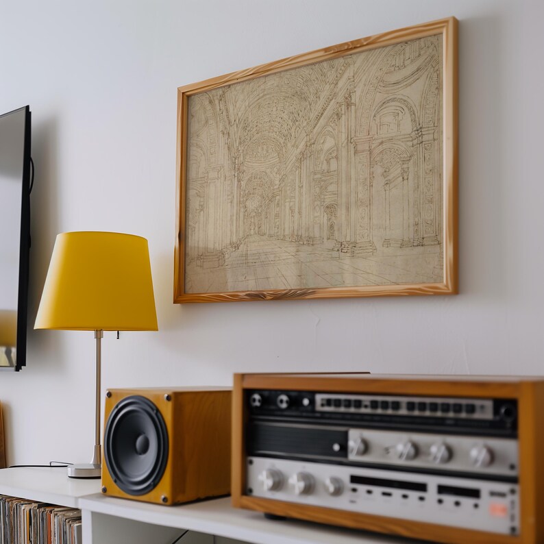 Op de afbeelding: Een ingelijste architectuurschets in een licht houten frame hangt boven een stereosysteem en een gele lamp. De schets toont een gedetailleerd interieur met bogen en kolommen. Het stereosysteem heeft een houten behuizing en zilveren componenten.