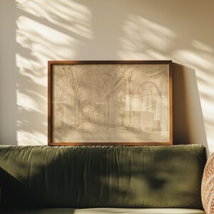 Op de afbeelding: Een ingelijste architectuurschets in een warmbruine houten lijst. De schets toont een lang, gewelfd interieur met gedetailleerde bogen en kolommen. Het kunstwerk wordt tentoongesteld boven een groene fluwelen bank, met schaduwen van zonlicht.
