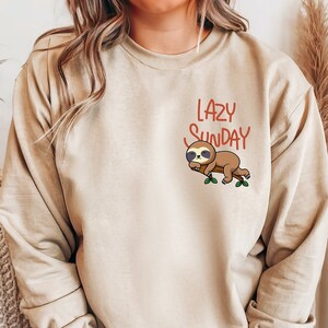 May include: A beige sweatshirt with a sloth graphic and the text "LAZY SUNDAY" in brown lettering.