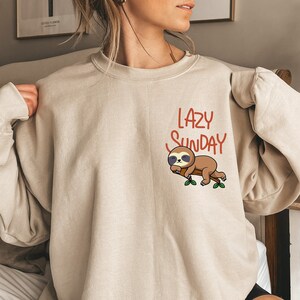May include: A beige sweatshirt with a graphic of a sloth sleeping on a branch with the text "Lazy Sunday" printed on it.