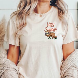 May include: A white t-shirt featuring a brown sloth wearing sunglasses and the text "Lazy Sunday" in red.