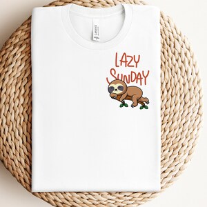 May include: White t-shirt featuring a brown sloth sleeping on a branch with green leaves. The text "LAZY SUNDAY" is written in orange above the sloth.