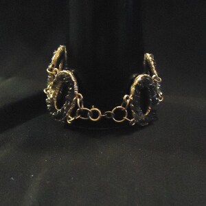 Peut inclure: Un bracelet en cha&icirc;ne dor&eacute;e avec des perles de verre noires et vertes. Les perles sont de forme ovale et sont reli&eacute;es par une cha&icirc;ne dor&eacute;e.