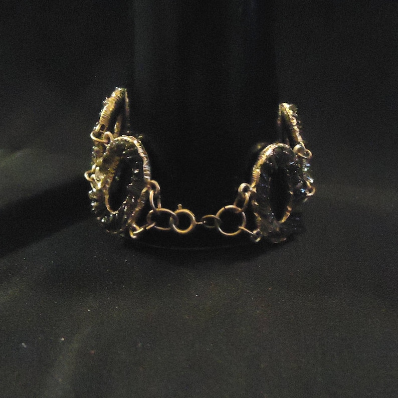 Peut inclure: Un bracelet en cha&icirc;ne dor&eacute;e avec des perles de verre noires et vertes. Les perles sont de forme ovale et sont reli&eacute;es par une cha&icirc;ne dor&eacute;e.