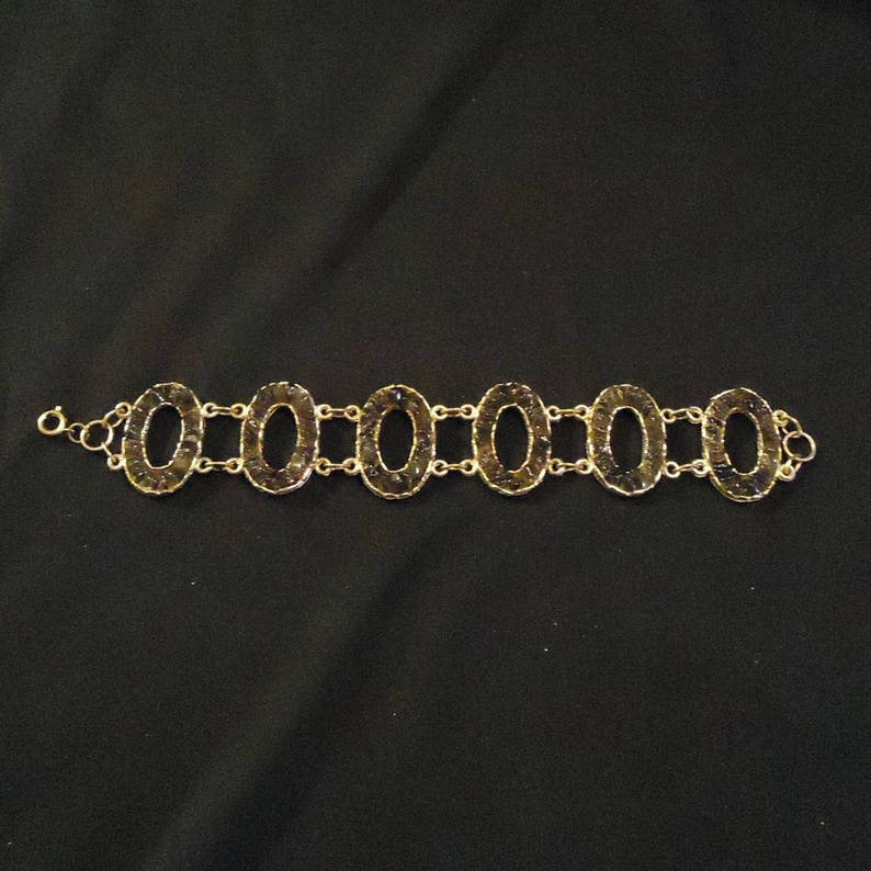 Peut inclure: Un bracelet en or avec des maillons ovales, chacun rempli de petites pierres brun fonc&eacute;.