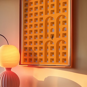 Könnte beinhalten: Ein gerahmter Druck eines abstrakten geometrischen Designs in Orange- und Blautönen. Das Design zeigt ein Gitter aus Quadraten mit ausgeschnittenen Bögen, wodurch ein Gefühl von Tiefe und Perspektive entsteht.