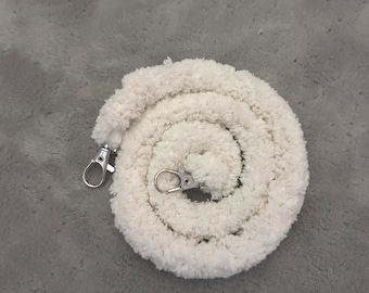 May include: A coiled, off-white, fluffy rope with two silver-colored metal swivel clasps. The rope is made of a soft, textured material and is arranged in a spiral shape. The clasps are attached at each end.
