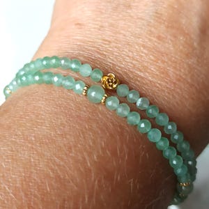 Peut inclure: Bracelet à deux rangs avec des perles de pierres précieuses vert clair. Un charm en forme de rose doré et de petites perles dorées ornent le bracelet. Le bracelet est conçu pour être porté au poignet.