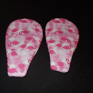 May include: A pair of pink oven mitts with a flamingo print. The mitts are made of fabric and have a quilted design.