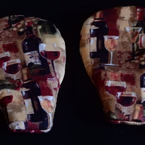 May include: Two wine-themed fabric pot holders with a red, brown, and beige background. The pot holders feature a repeating pattern of wine bottles and glasses.