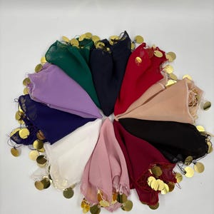 Puede incluir: Una colección de coloridas bufandas de gasa dispuestas en un patrón circular. Cada bufanda es de un color diferente, incluyendo verde, morado, azul marino, rojo y rosa. Monedas doradas están unidas a los bordes de las bufandas, agregando un elemento decorativo.