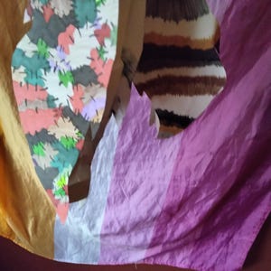 May include: Abstract art piece featuring a colorful patchwork design with various leaf shapes in shades of red, green, and gray. The background includes a striped pattern in brown and white, and a draped fabric in shades of yellow, white, and purple.