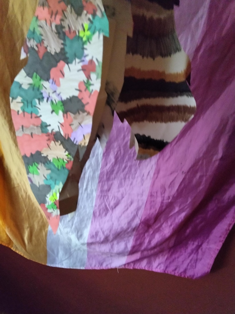 May include: Abstract art piece featuring a colorful patchwork design with various leaf shapes in shades of red, green, and gray. The background includes a striped pattern in brown and white, and a draped fabric in shades of yellow, white, and purple.