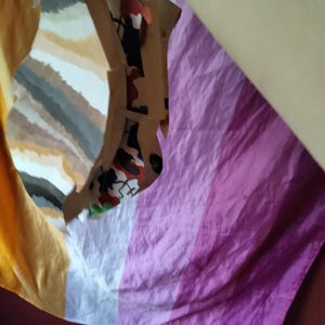 May include: A folded fabric with a color block design. The fabric has a striped pattern in shades of yellow, white, gray, and brown. Another section of the fabric has vertical stripes in shades of pink and purple.