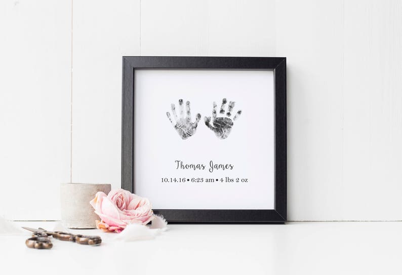 May include: Black framed print with two handprints in gray ink. The print includes the name "Thomas James", the date "10.11.16", the time "6:23 am", and the weight "4 lbs 2 oz".