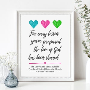May include: A white framed print with a black cursive quote that reads "For every lesson you've prepared, the love of God has been shared."  Three hearts are at the top of the print, one blue, one pink, and one green. The text below the quote reads "Mr. Larry & Ms. Sandi Aument, Pine Level United Methodist Church, Children's Ministry."