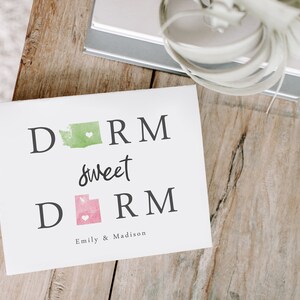 May include: A white card with the text "Dorm sweet dorm" in black lettering. The states of Washington and Utah are depicted in green and pink watercolor, respectively, with a small white heart in each state. The card is signed "Emily & Madison".
