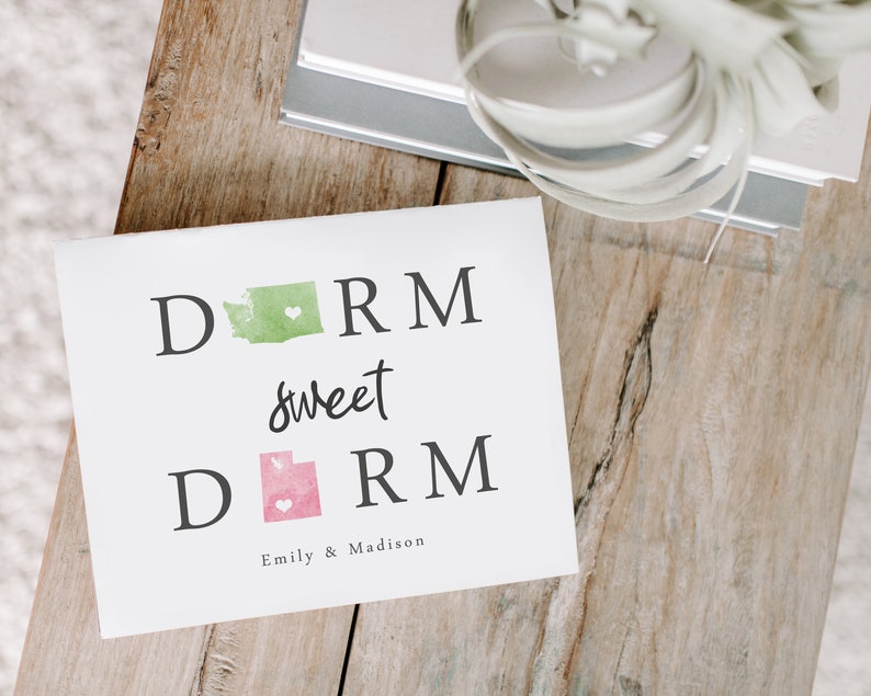 May include: A white card with the text "Dorm sweet dorm" in black lettering. The states of Washington and Utah are depicted in green and pink watercolor, respectively, with a small white heart in each state. The card is signed "Emily & Madison".