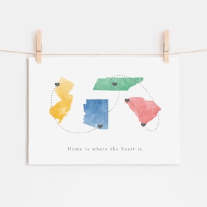 May include: A watercolour print featuring the states of New Jersey, Tennessee, Arizona, and South Carolina. Each state is outlined in a different colour and has a small black heart in the centre. The states are connected by a dotted line and the text "Home is where the heart is." is printed below the states.
