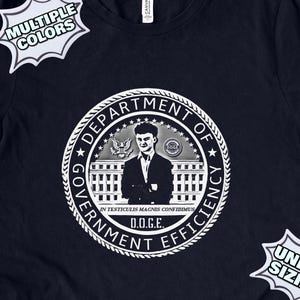 May include: A navy blue t-shirt with a white graphic of a seal that says "Department of Government Efficiency" with a man in a suit and tie inside the seal. The text "D.O.G.E." is below the seal.