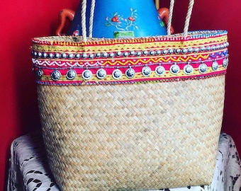 May include: A woven straw tote bag with a colorful beaded trim. The bag has a rope handle and is decorated with silver and gold beads.