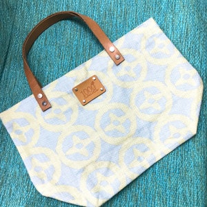 May include: A light blue tote bag with a brown leather handle and a brown leather patch with the text "1000 Islands" on it. The bag has a white and light blue geometric pattern.