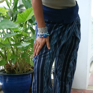Pu&ograve; includere: Pantaloni a righe blu e bianche con una cintura blu scuro. I pantaloni sono realizzati in un tessuto morbido e fluido e hanno una vestibilit&agrave; rilassata. La persona indossa diversi braccialetti al polso, tra cui un braccialetto rigido d'argento e un braccialetto di perline.