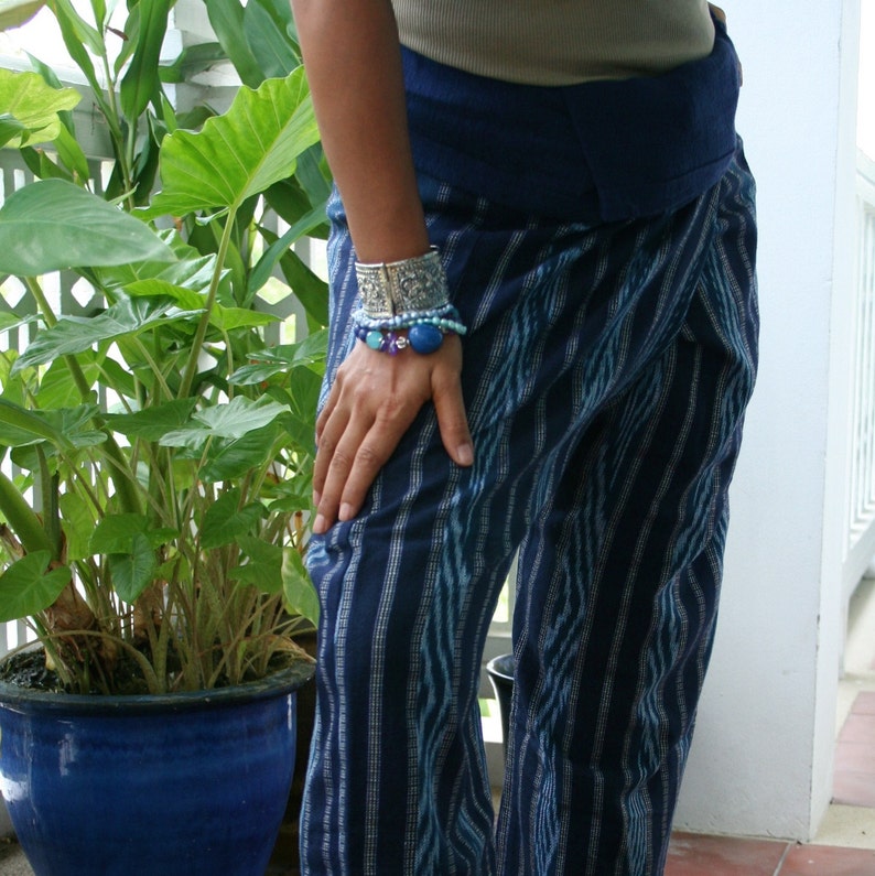 Pu&ograve; includere: Pantaloni a righe blu e bianche con una cintura blu scuro. I pantaloni sono realizzati in un tessuto morbido e fluido e hanno una vestibilit&agrave; rilassata. La persona indossa diversi braccialetti al polso, tra cui un braccialetto rigido d'argento e un braccialetto di perline.