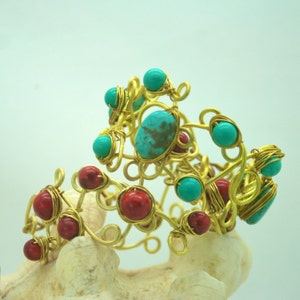 May include: A gold wire bracelet with turquoise and red stones. The bracelet is made of wire that is twisted and shaped into a delicate design. The stones are set in the wire and are held in place by the wire.