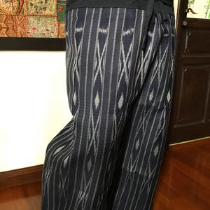 Pu&ograve; includere: Un paio di pantaloni a righe blu e bianche con un motivo geometrico. I pantaloni sono legati in vita con una fascia blu scuro.