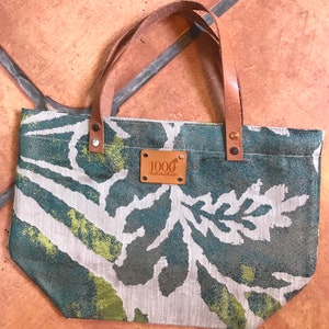 May include: A small green and white tote bag with a brown leather handle and a brown leather patch that says "1000 roads".