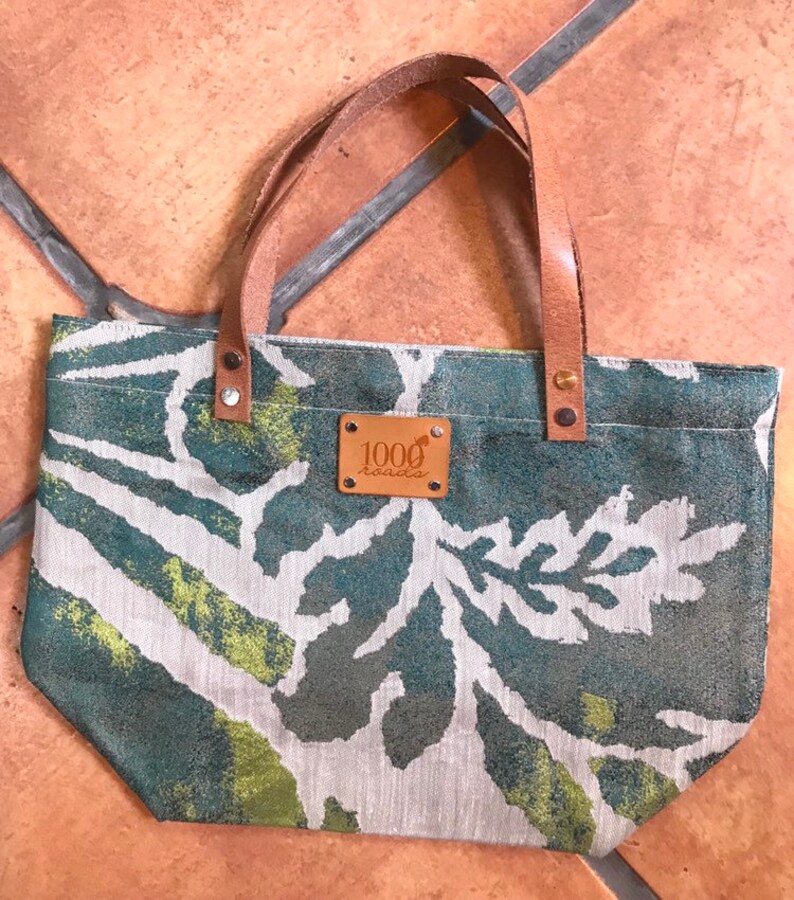 May include: A small green and white tote bag with a brown leather handle and a brown leather patch that says "1000 roads".