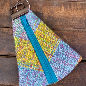 May include: A small, triangular zippered pouch with a colorful woven fabric exterior. The pouch has a blue zipper and a silver metal key ring.