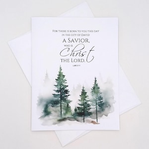 May include: A white greeting card with the text "FOR THERE IS BORN TO YOU THIS DAY IN THE CITY OF DAVID A SAVIOR, WHO IS Christ THE LORD. LUKE 2:11." The card features a watercolor painting of evergreen trees in a misty forest.