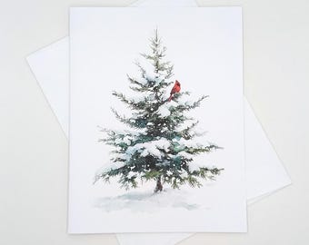 May include: A watercolor illustration of a snow-covered evergreen tree with a bright red cardinal perched on a branch. The image is on a white card with a matching envelope, evoking a winter or holiday theme.