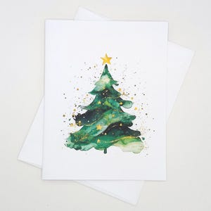 May include: A watercolor Christmas card featuring a green Christmas tree with gold accents and a gold star on top. The tree is decorated with gold stars and gold paint splatters. The card is on a white background with a white envelope.