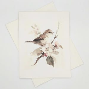May include: A rectangular greeting card featuring a watercolor illustration of a small brown bird perched on a flowering branch. The bird has soft brown and cream plumage, and the branch displays delicate white blossoms and green leaves.