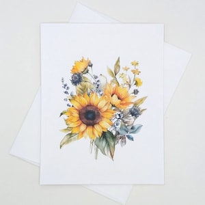May include: A greeting card featuring a watercolor illustration of sunflowers and other wildflowers. The bouquet includes yellow sunflowers with brown centers, blue thistle, and green leaves. The card is white, with a matching white envelope.