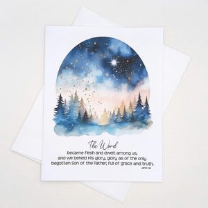 May include: A greeting card with a watercolor painting of a starry night sky over a forest. The image is framed by an arch shape. The text "The Word" and a Bible verse are printed below the image. The card is white.