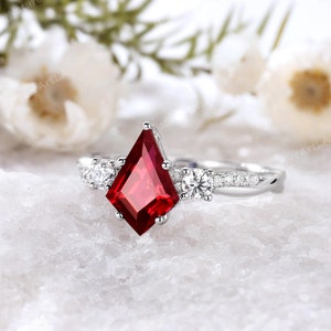 Peut inclure: Une bague en argent avec une grande pierre précieuse rouge en forme de cerf-volant entourée de petites pierres précieuses blanches.
