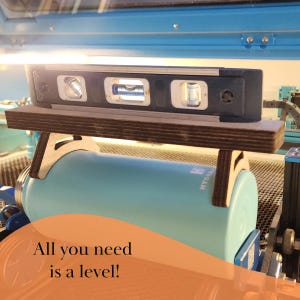 K&ouml;nnte beinhalten: Eine Wasserwaage liegt auf einem Holzst&auml;nder, der zum Ausrichten einer blauen Wasserflasche verwendet wird. Der Text "All you need is a level!" ist auf einem pfirsichfarbenen Hintergrund geschrieben.
