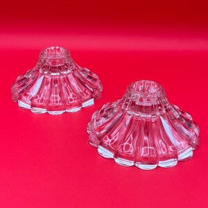 May include: Two clear glass candle holders with a fluted design. The holders are on a red background.