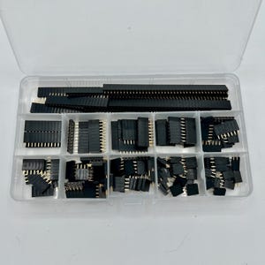 May include: A clear plastic organizer filled with various black and gold electronic components. The components include male and female header pins, and connectors. The organizer is divided into multiple compartments, each holding a different type of component.