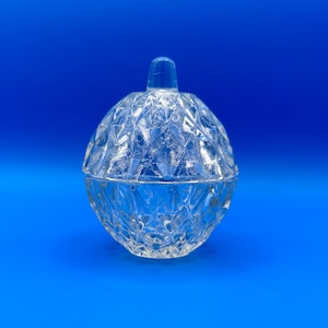 May include: A clear glass jar with a lid, shaped like a sphere with a diamond pattern. The jar is on a blue background.