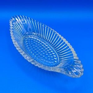 May include: A clear glass serving dish with a ribbed design and a textured bottom. The dish is oval shaped and has a slight curve.