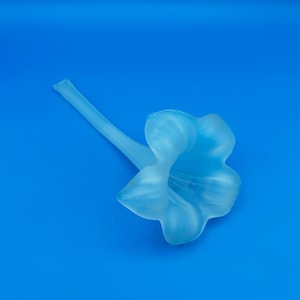May include: A light blue, frosted glass flower with a long stem. The flower has a trumpet shape with multiple petals. The object is set against a solid blue background.