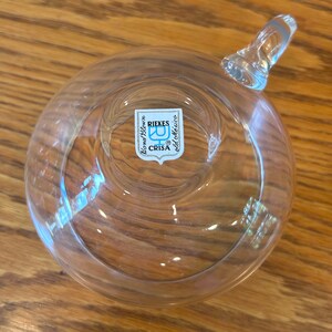May include: A clear glass cup with a handle. The cup has a sticker on the bottom that reads "Handblown, RIEKES, CRISA, old collection".
