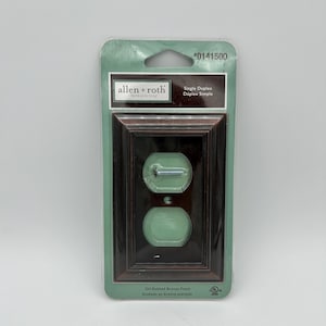 May include: An oil-rubbed bronze finish single duplex electrical outlet cover. The cover is in a clear plastic package with the brand name "allen + roth" and product information printed on the packaging.