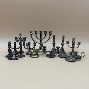 May include: A selection of antique brass and bronze candle holders in various shapes and sizes. The collection includes multi-arm candelabras, single candlesticks, and decorative holders, all with a vintage aesthetic.