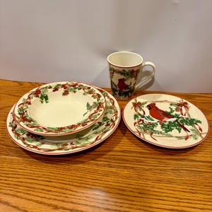 Puede incluir: Un juego de vajilla con temática navideña con un diseño de pájaro cardenal. El juego incluye una taza, un cuenco y dos platos. Los platos y el cuenco tienen un borde rojo y verde con acebo y cintas.